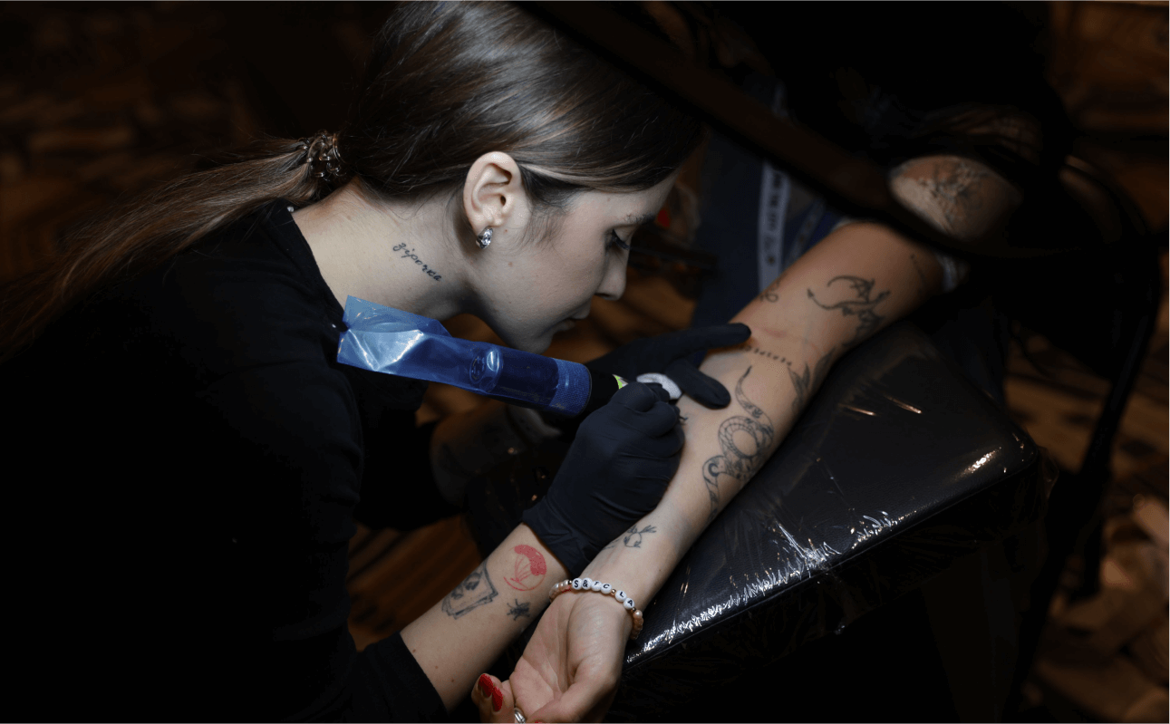 Tattoo artist applying a delicate tattoo to the bride at a wedding, capturing the essence of the celebration with custom inked artwork.